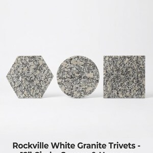 Puede incluir: Tres salvamanteles de granito blanco Rockville en forma hexagonal, circular y cuadrada. Cada pieza presenta una textura de piedra moteada gris y blanca. El texto dice: Rockville White Granite Trivets - 12" Circle, Square & Hexagon.