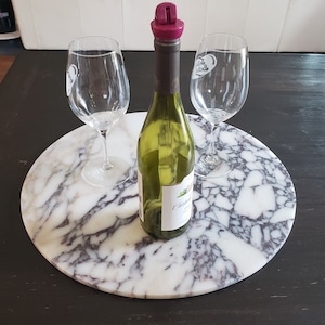 May include: A white marble serving tray with a purple swirl pattern. Two clear wine glasses and a bottle of white wine with a purple stopper are on the tray.