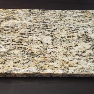 May include: A square, light brown granite countertop with a speckled pattern of black and red flecks.
