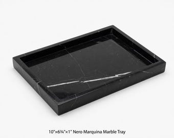 May include: A rectangular Nero Marquina marble tray, measuring 10" x 6.75" x 1", with a polished black surface and white veining. The tray has a raised edge and is suitable for various uses.