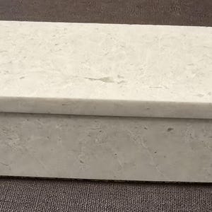 Puede incluir: Una caja rectangular blanca con una superficie texturizada. La caja est&aacute; hecha de un material que se asemeja al m&aacute;rmol.