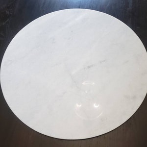 May include: A white round marble serving tray with a smooth surface.