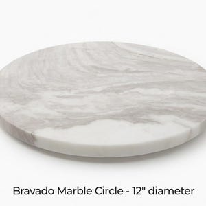May include: A circular Bravado Marble Circle, 30 cm in diameter, with a white and grey marbled pattern. The stone surface has a smooth finish. The product is a decorative item.