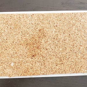 May include: A close-up of a cork board with a white frame. The cork board is made of natural cork and has a slightly rough texture.