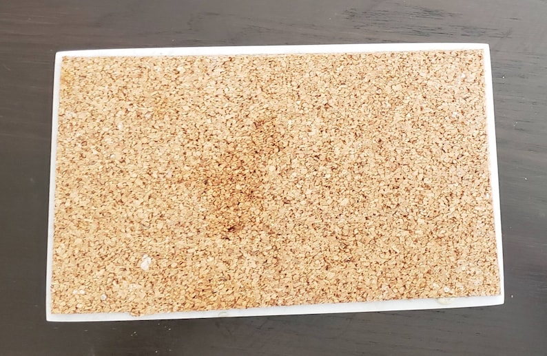 May include: A close-up of a cork board with a white frame. The cork board is made of natural cork and has a slightly rough texture.