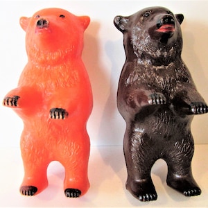May include: Two toy bears standing upright. The bear on the left is orange and the bear on the right is brown.