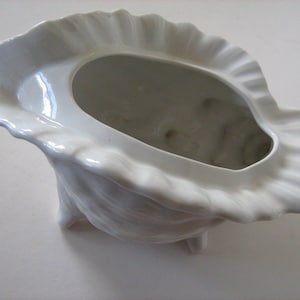 May include: White ceramic shell-shaped serving dish with a fluted rim. The dish is empty and ready to be filled.