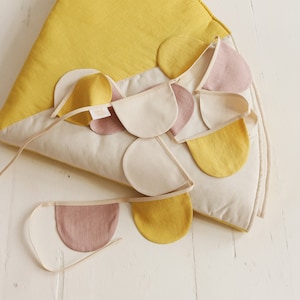 May include: A yellow, cream, and pink fabric play mat with a circle design. The mat is made of soft, natural materials and is perfect for babies and toddlers. The mat is made by the company "mini mini".