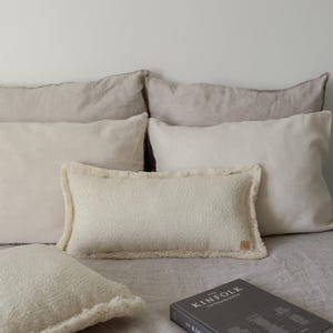 Könnte beinhalten: Ein Bett mit einem weißen, flauschigen Kissen und einem Buch mit dem Titel "The Kinfolk Entrepreneur" auf einem weißen Leinenlaken. Das Bett ist mit mehreren beigefarbenen und cremefarbenen Kissen dekoriert.