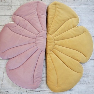 May include: A large, flower-shaped play mat with two halves, one pink and one yellow. The mat is made of soft, quilted fabric and has a scalloped edge.