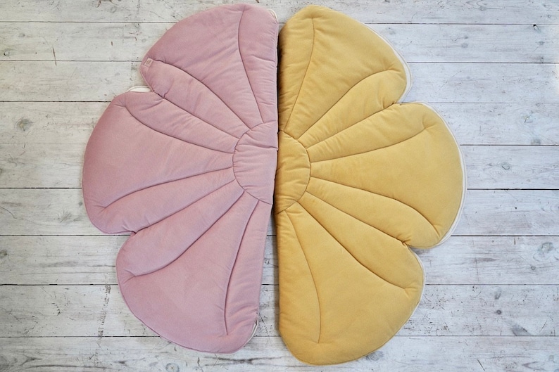 May include: A large, flower-shaped play mat with two halves, one pink and one yellow. The mat is made of soft, quilted fabric and has a scalloped edge.