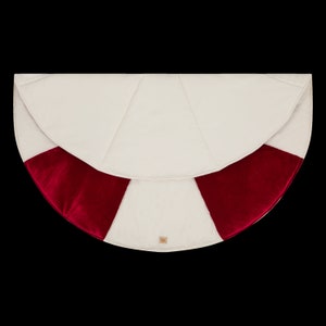 May include: A white and red Christmas tree skirt with a velvet trim. The skirt is round and has a scalloped edge.