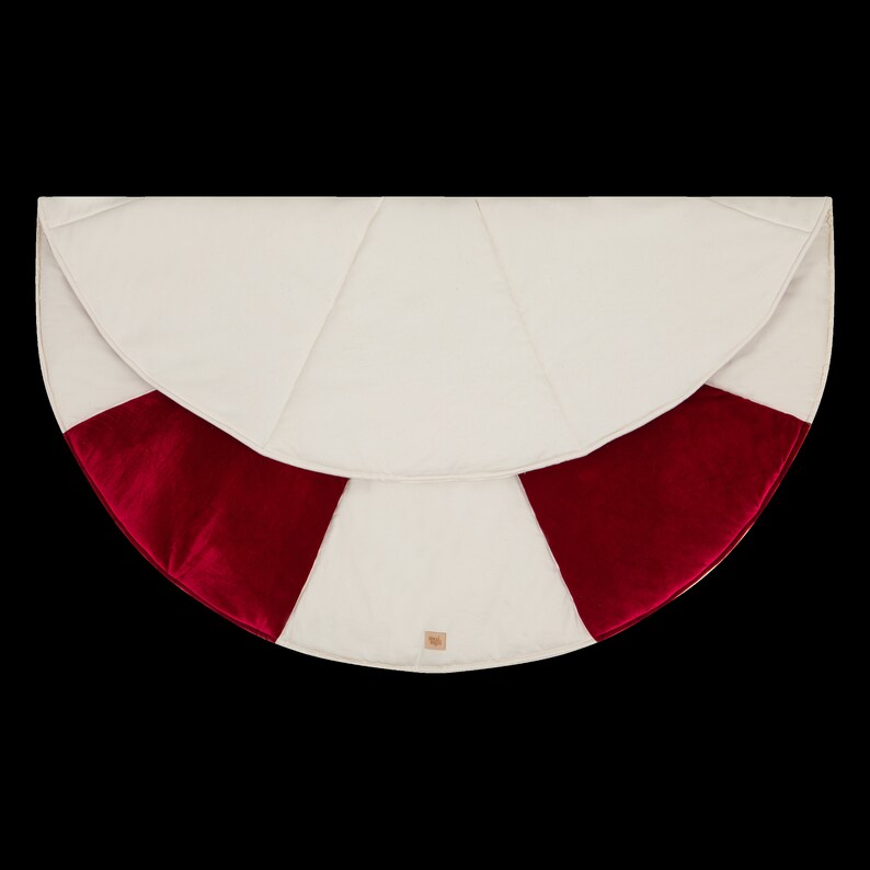 May include: A white and red Christmas tree skirt with a velvet trim. The skirt is round and has a scalloped edge.