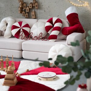 May include: A white sofa with red and white candy cane cushions, a red stocking, and a red "ho ho ho" sign. The sofa is in a room with a white and red play mat on the floor.