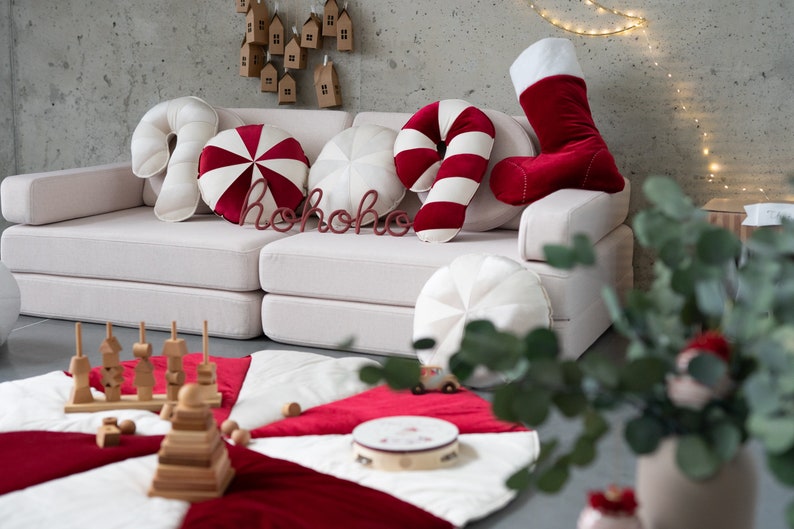 May include: A white sofa with red and white candy cane cushions, a red stocking, and a red "ho ho ho" sign. The sofa is in a room with a white and red play mat on the floor.