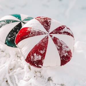 Peut inclure: Deux coussins ronds avec un motif en spirale. Le coussin de gauche est bleu sarcelle et blanc, et le coussin de droite est rouge et blanc. Les deux coussins sont recouverts d'une fine couche de neige.
