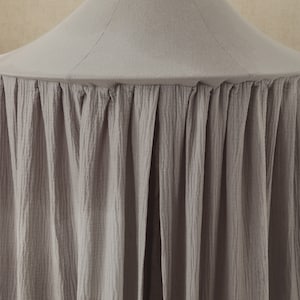 May include: A gray fabric canopy with a ruffled edge. The canopy is made of a soft, textured fabric and is perfect for creating a cozy and private space.