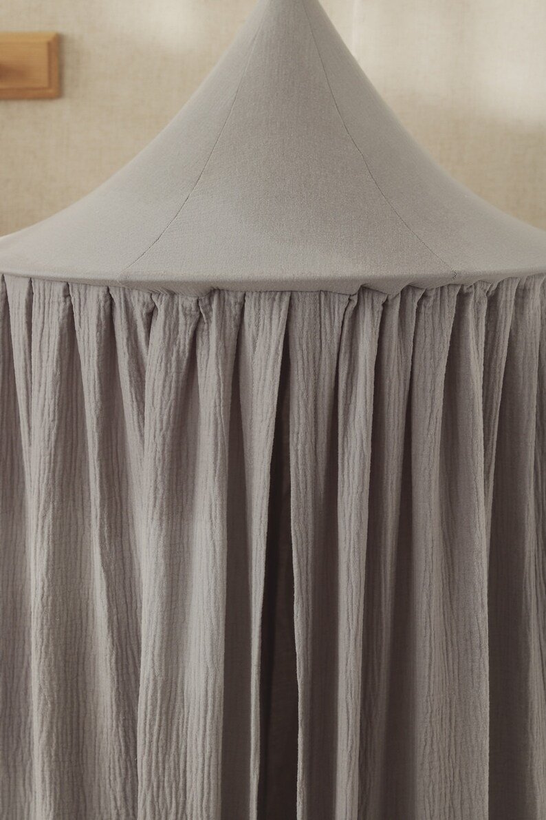 May include: A gray fabric canopy with a ruffled edge. The canopy is made of a soft, textured fabric and is perfect for creating a cozy and private space.