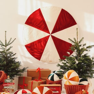 May include: A red and white candy cane-shaped Christmas tree skirt with a red velvet texture.  There are several small Christmas trees, wrapped gifts, and red, white, and orange candy cane-shaped pillows on the floor.  The sign reads "North Pole, Santa's Workshop, Ho-Ho-Ho, My Room."