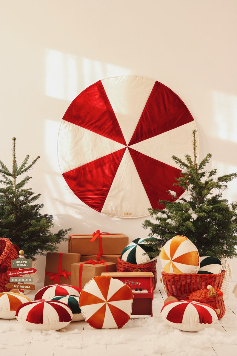 May include: A red and white candy cane-shaped Christmas tree skirt with a red velvet texture.  There are several small Christmas trees, wrapped gifts, and red, white, and orange candy cane-shaped cushions on the floor.  The sign reads "North Pole, Santa's Workshop, Ho-Ho-Ho, My Room."