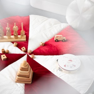 May include: A white and red play mat with a wooden toy stacking pyramid, a wooden toy with different shapes, a wooden toy car, and a tambourine with a Santa Claus design and the text "Merry Christmas".