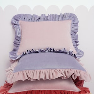 May include: A stack of four decorative cushions with ruffled edges. The cushions are in shades of pink, lavender, and red.