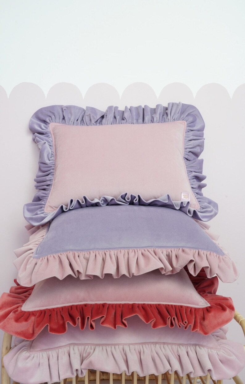 May include: A stack of four decorative cushions with ruffled edges. The cushions are in shades of pink, lavender, and red.