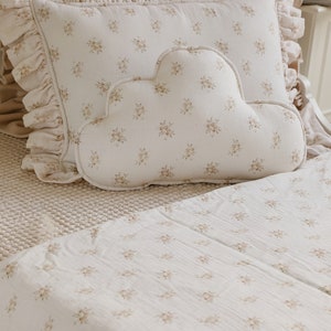 Könnte beinhalten: Ein weißes, wolkenförmiges Kissen mit Blumenmuster liegt auf einem weißen Bett mit Blumenmuster. Das Kissen hat einen gekräuselten Rand.