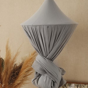 May include: A gray cotton canopy hanging from the ceiling. The canopy is gathered at the bottom and tied in a knot.