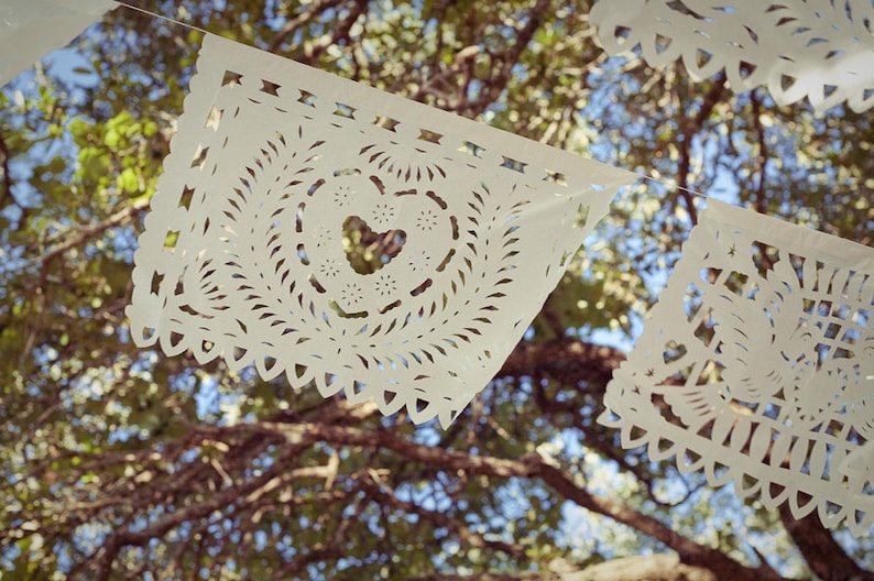May include: White paper cutouts with intricate designs hang from a tree branch. The cutouts are shaped like squares with rounded corners and feature a heart shape in the center.