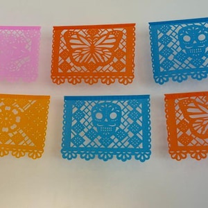 May include: Six rectangular paper banners featuring intricate die-cut designs including butterflies, skulls, and floral patterns. The banners are colored in pink, orange, yellow, and blue, each with a scalloped bottom edge and geometric cutouts.