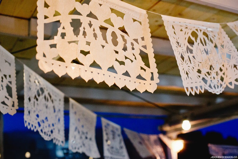 May include: White paper cutouts with intricate designs, including hearts and flowers, are strung together to form a festive banner. One cutout features the word "AMOR" in a decorative font.