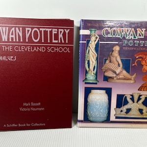 May include: Two books about Cowan Pottery. The book on the left is red with white text that reads "COWAN POTTERY AND THE CLEVELAND SCHOOL WITH VALUES". The book on the right has a purple cover with images of pottery and the text "COWAN POTTERY IDENTIFICATION & VALUES".