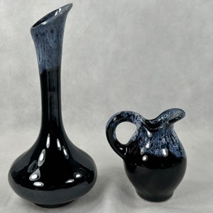 May include: Two black ceramic vases with a blue and white glaze. The larger vase is tall and slender with a flared base. The smaller vase is round with a handle.