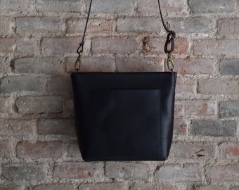 Kleine Crossbody-tasche aus schwarzem Leder mit Außentasche und Reißverschluss. Handarbeit.