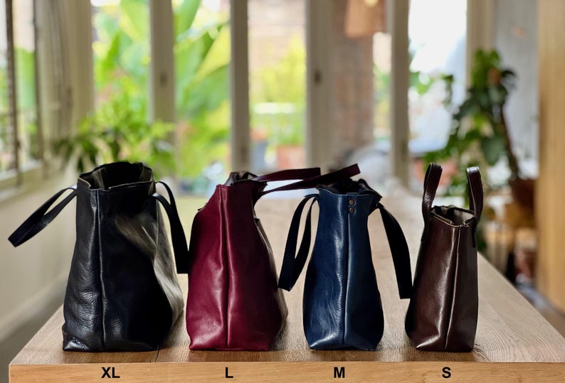 May include: Four leather tote bags in different sizes, from left to right: XL, L, M, and S. The bags are black, burgundy, navy blue, and brown.