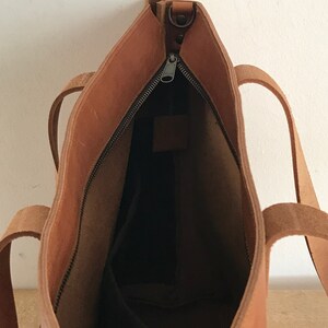 May include: A brown leather tote bag with a zipper closure. The bag is open and the inside is visible. The bag has two straps.