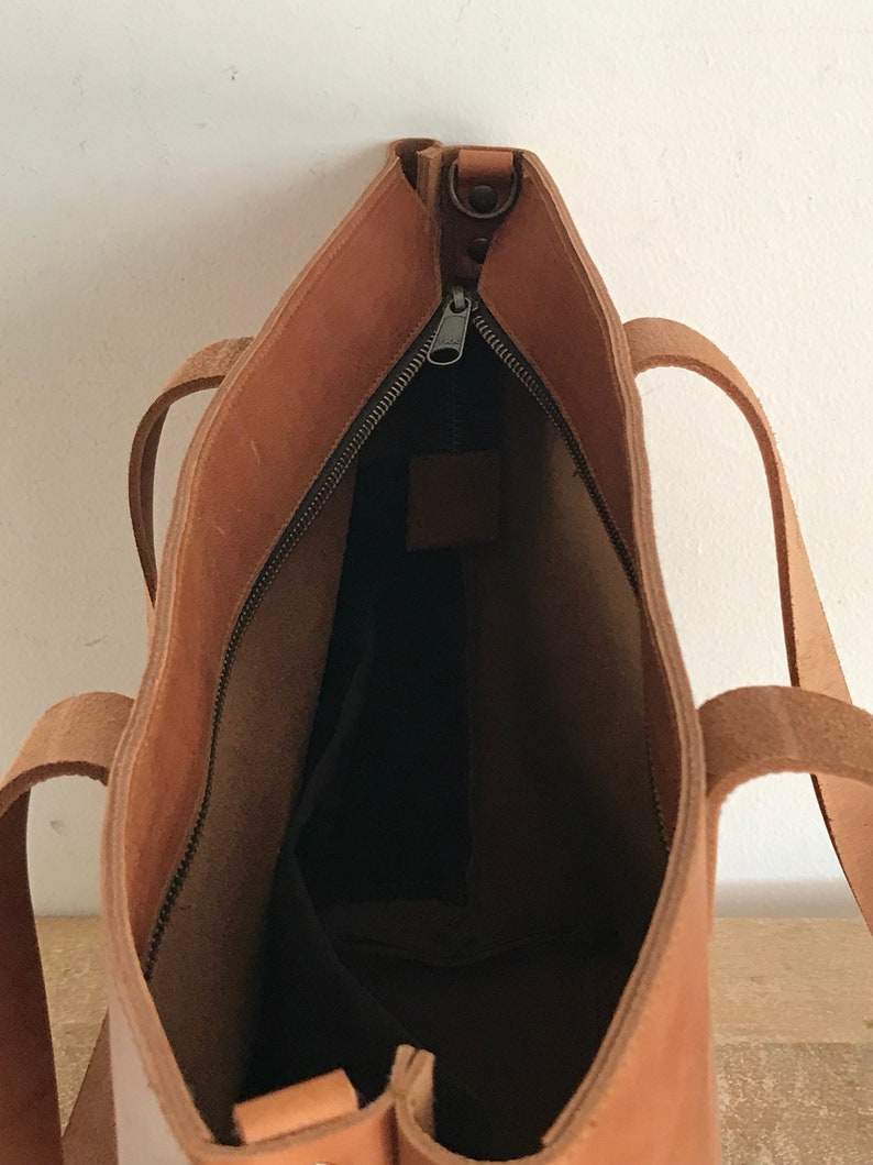 May include: A brown leather tote bag with a zipper closure. The bag is open and the inside is visible. The bag has two straps.