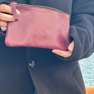 May include: A burgundy leather zippered pouch with a small leather strap.