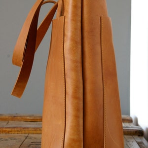 May include: A large, brown leather tote bag with two long handles. The bag has a simple, classic design and is made of high-quality leather.