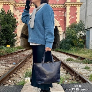 May include: A blue cardigan with a gray scarf worn by a person standing on a railroad track. The person is holding a black leather tote bag. Size M on a 5'1" person (156 cm).