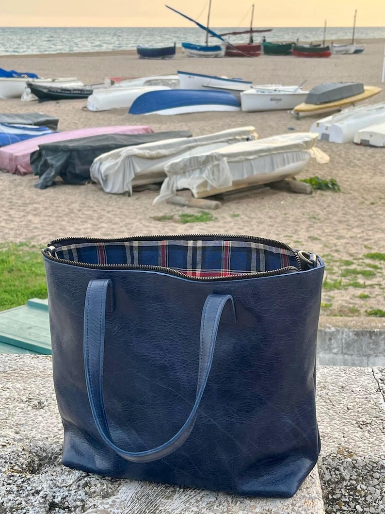May include: A blue leather tote bag with a plaid lining. The bag has two handles and a zipper closure.