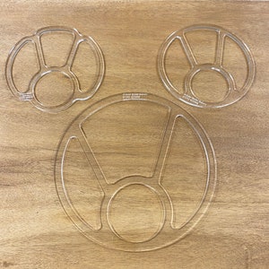 May include: Three clear plastic stencils for painting or crafting. The stencils are circular and feature different designs with multiple sections. The stencils are labelled "Artist Made Makers" and have a website address.