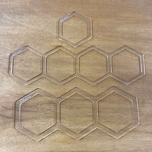 May include: A set of six clear acrylic hexagon-shaped stencils. The stencils are arranged in a honeycomb pattern. The stencils are labelled "Artisan Model Makers 07743 807546".