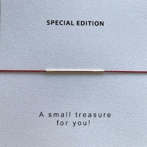 May include: A minimalist bracelet featuring a thin gold bar centered on a red cord. The text "SPECIAL EDITION" is printed above the bracelet, and the text "A small treasure for you!" is printed below.