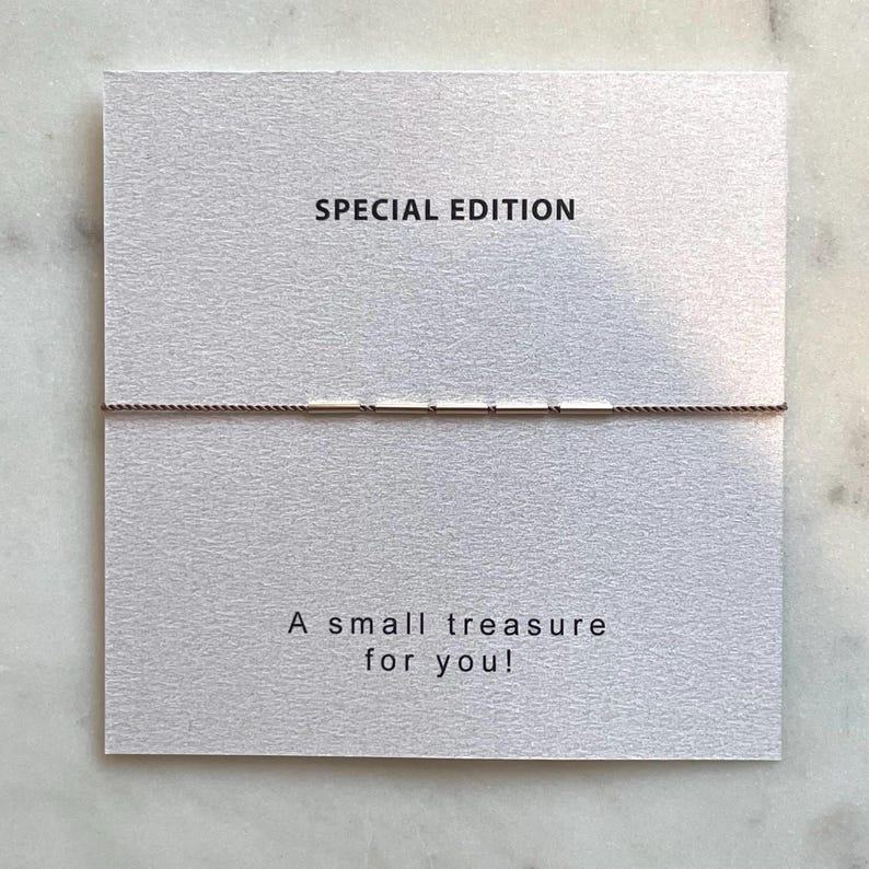 May include: A small treasure for you! is printed on a white card with a thin brown string bracelet. The words "SPECIAL EDITION" are printed at the top of the card. The background is a light gray marble.