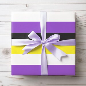 Puede incluir: Una caja de regalo envuelta en rayas moradas, negras, amarillas y blancas con una cinta de satén blanca atada en un lazo.