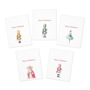 May include: Five white rectangular greeting cards, each featuring the red text Merry Christmas and a watercolor illustration. The designs include a gold nutcracker, a green nutcracker, a ballerina in a green dress, a mouse king, and a pink nutcracker.