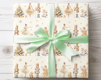 May include: A white gift wrap with a repeating pattern of ballerinas, nutcrackers, and a Christmas tree. The gift wrap is tied with a light green ribbon.