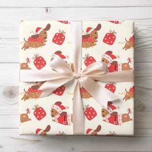 May include: A wrapped gift with cream-colored wrapping paper featuring a repeating pattern of dachshunds in Santa hats and red gift boxes. The gift is tied with a cream-colored satin ribbon and bow.
